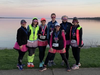 seven women in pink tutus at the edge of a lake as the sun sets