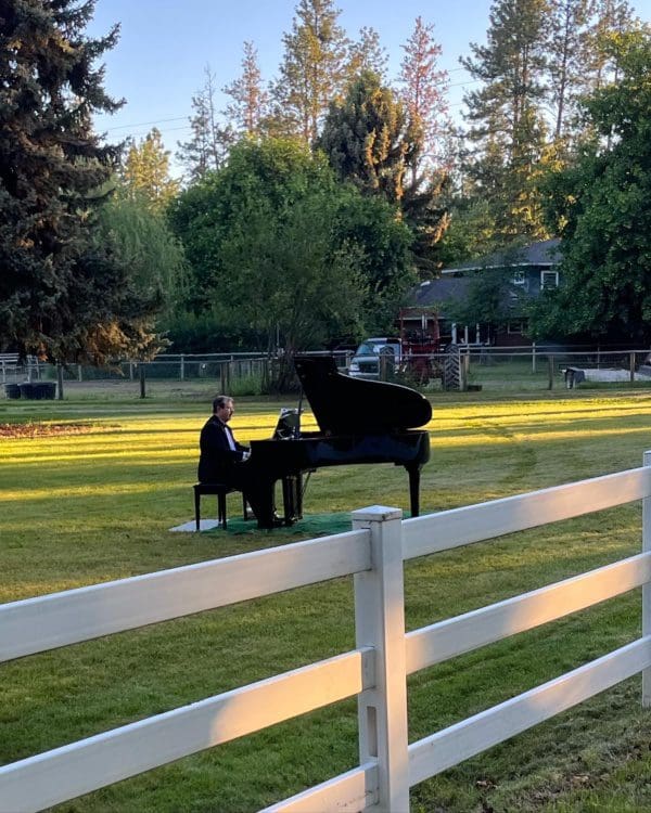 Dude playing a baby grand piano on his front lawn.