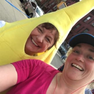 A woman in a blue running hat poses with a woman in a banana suit.