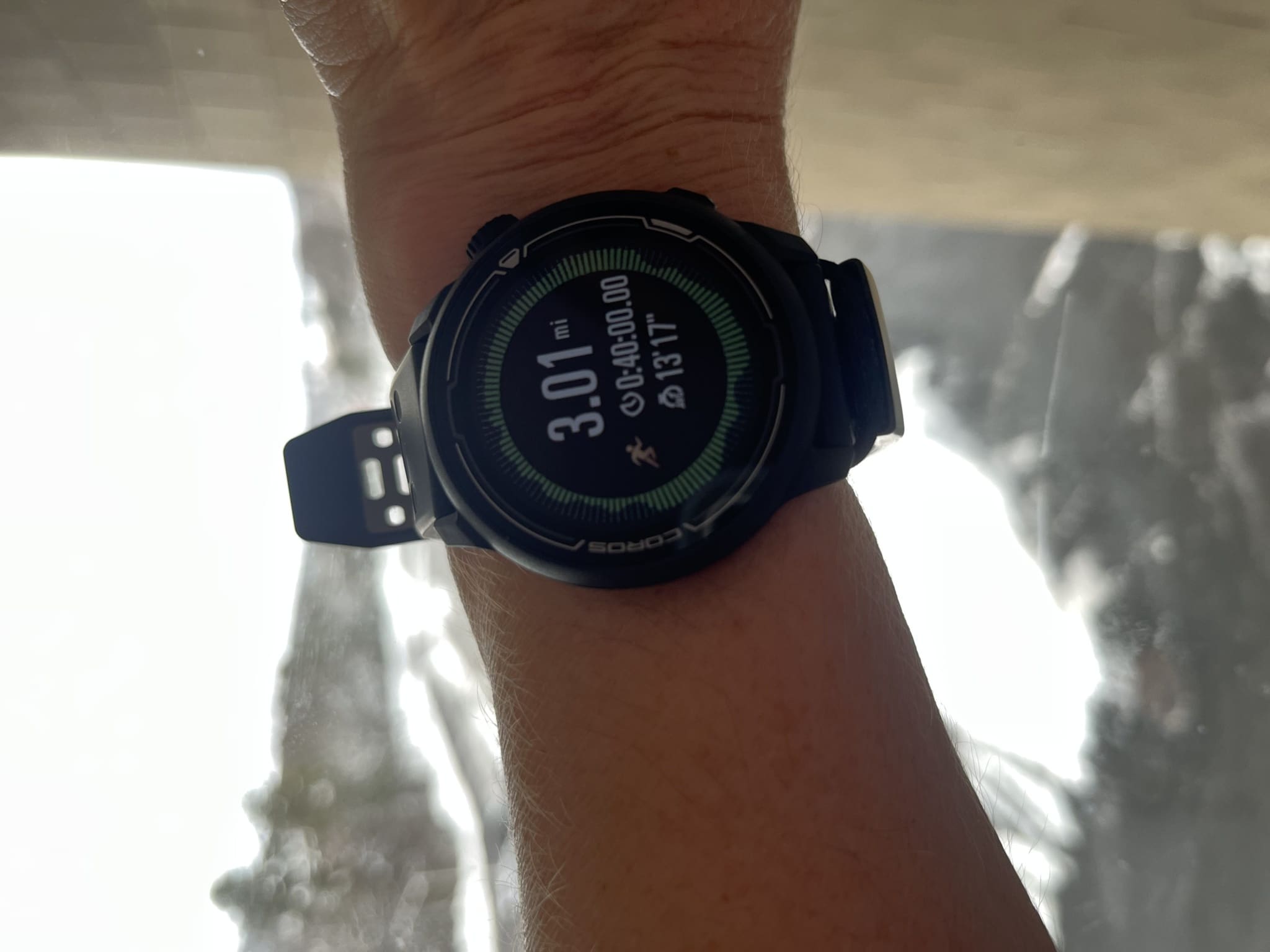 A woman's wrist with a running watch on it in front of a snowy landscape.