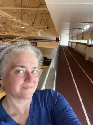 A grey haired woman is looking into the camera and indoor track lanes fill the right half of the image