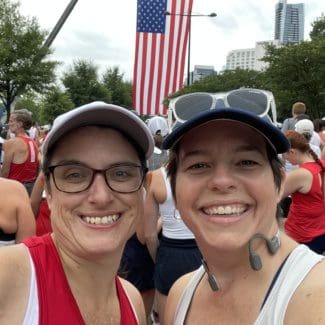 Two smiling women runners taking a selfie in front of a huge American flag